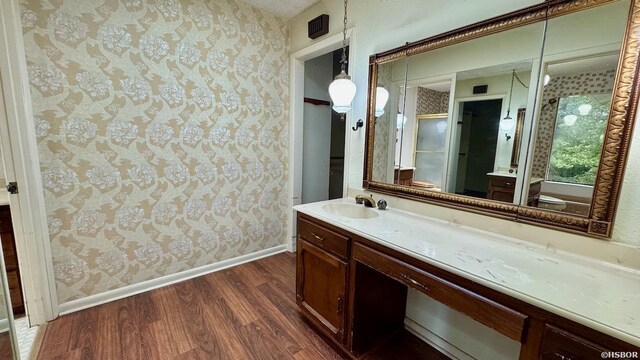 bathroom featuring vanity, a shower stall, wood finished floors, baseboards, and wallpapered walls