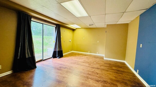 empty room with a drop ceiling, baseboards, and wood finished floors