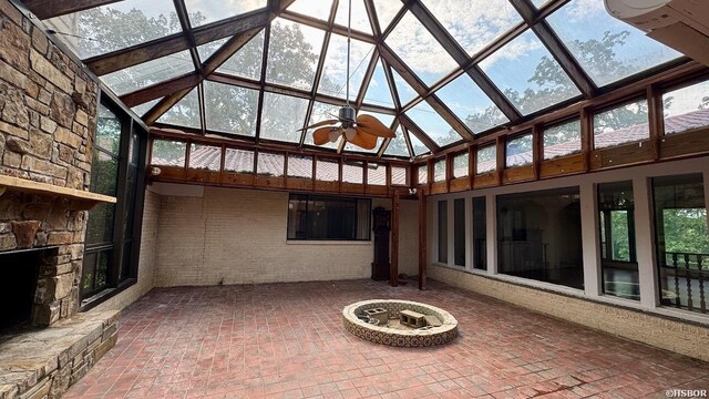 unfurnished sunroom featuring ceiling fan, a stone fireplace, a skylight, and a wealth of natural light