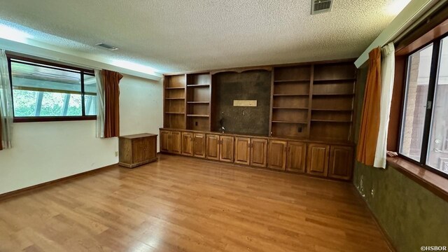 unfurnished living room featuring a textured ceiling, light wood finished floors, visible vents, and baseboards