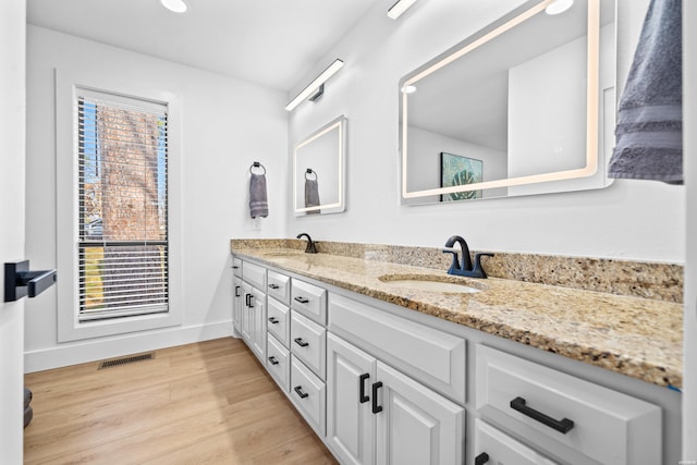 full bath with double vanity, a wealth of natural light, visible vents, a sink, and wood finished floors