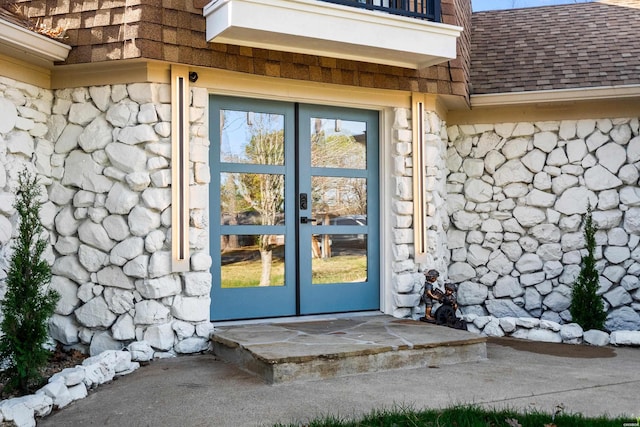 doorway to property featuring a shingled roof, stone siding, and french doors