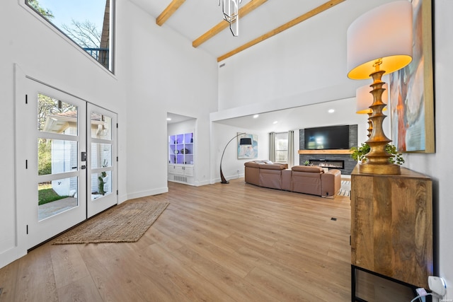 foyer with baseboards, a lit fireplace, french doors, light wood finished floors, and beamed ceiling