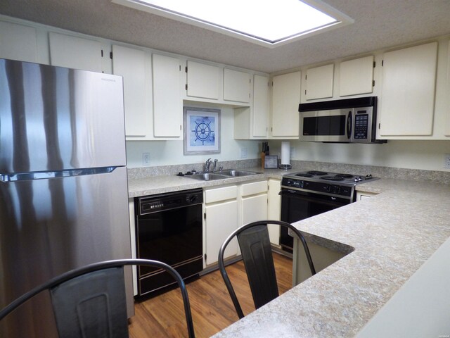 kitchen featuring white cabinets, dark wood-style flooring, light countertops, black appliances, and a sink