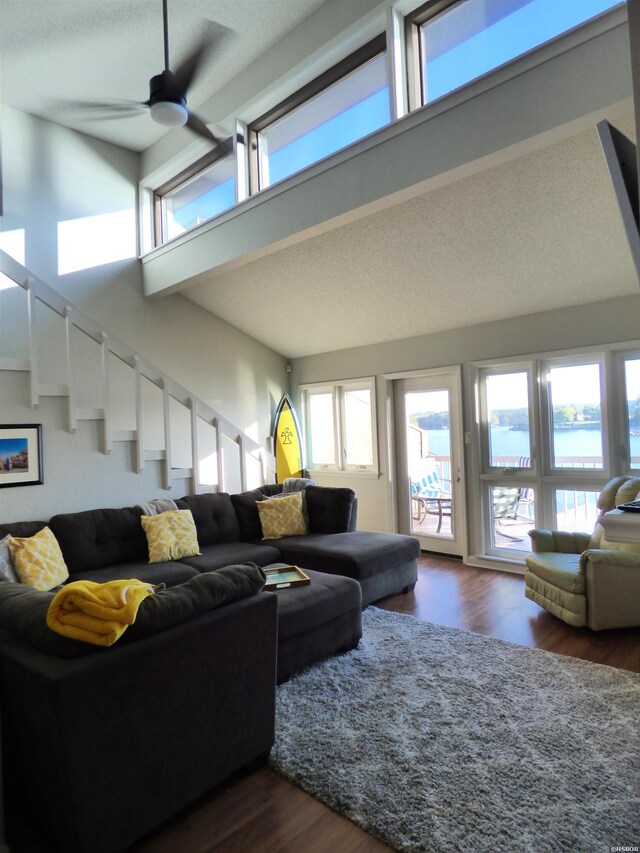 living area with ceiling fan, dark wood-type flooring, a water view, and a towering ceiling