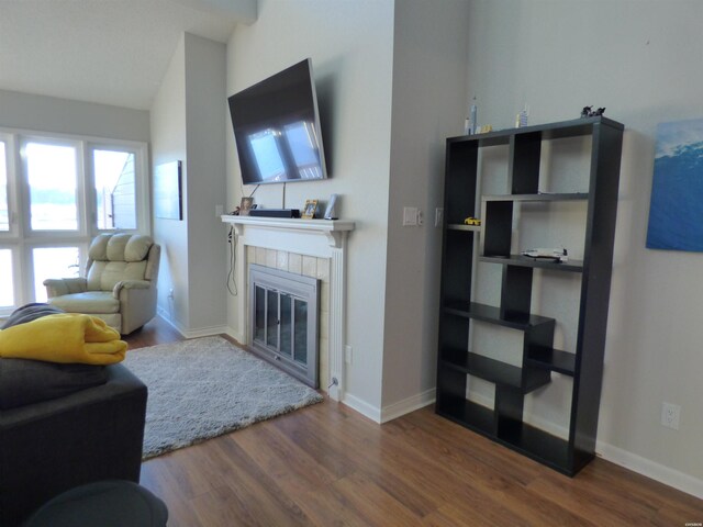 living area with a tiled fireplace, baseboards, vaulted ceiling, and dark wood-style flooring