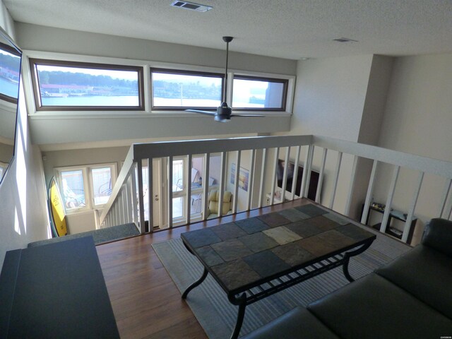 living room with a textured ceiling, dark wood-type flooring, visible vents, and a ceiling fan