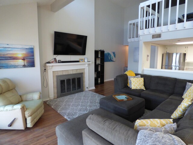 living room featuring dark wood-type flooring, a tile fireplace, visible vents, and high vaulted ceiling