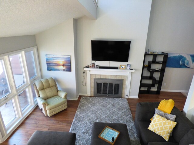 living room featuring lofted ceiling with beams, a tiled fireplace, baseboards, and dark wood-type flooring