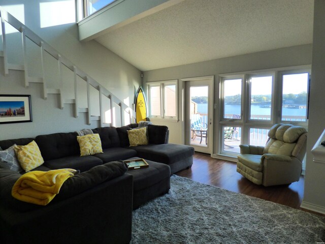 living area featuring a water view, dark wood-style floors, lofted ceiling with beams, and stairway