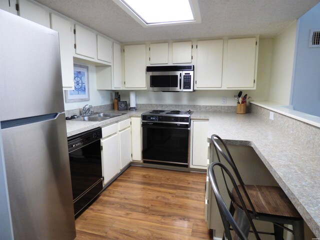 kitchen with white cabinets, black appliances, light countertops, and a sink