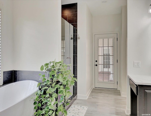 bathroom featuring baseboards, wood finished floors, vanity, a freestanding tub, and a shower stall