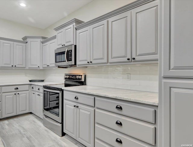 kitchen featuring appliances with stainless steel finishes, gray cabinetry, light wood-style floors, and decorative backsplash