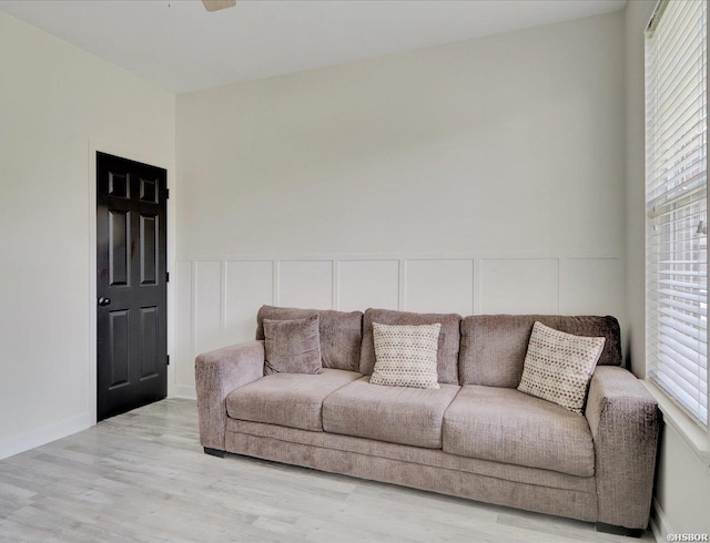 living room featuring light wood-style floors, a decorative wall, and wainscoting