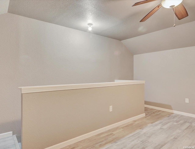 additional living space with vaulted ceiling, a textured ceiling, light wood-style flooring, and baseboards