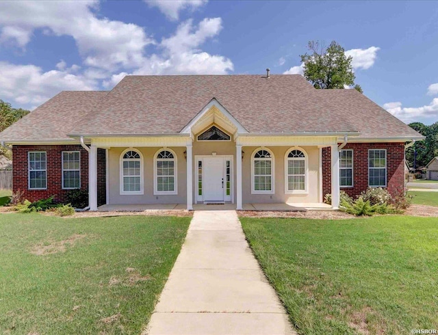 view of front of home with a shingled roof, brick siding, a front lawn, and stucco siding