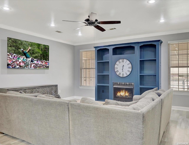 living area featuring light wood-style floors, a warm lit fireplace, visible vents, and crown molding