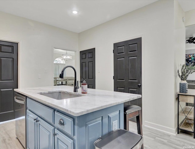 kitchen with an island with sink, light wood-style flooring, light stone counters, a sink, and stainless steel dishwasher