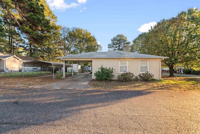 view of front facade featuring driveway, fence, a carport, and brick siding