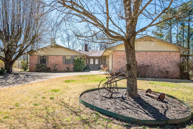 exterior space featuring brick siding, a lawn, driveway, and a chimney