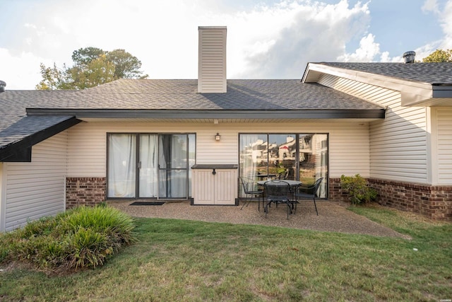 rear view of house with brick siding, a yard, a chimney, a patio, and a shingled roof