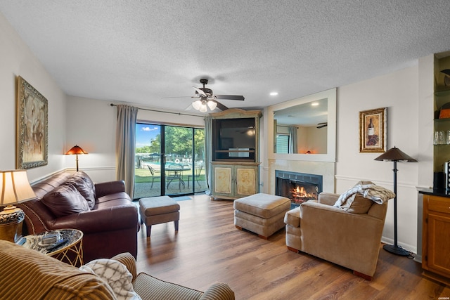 living area featuring a ceiling fan, a tile fireplace, a textured ceiling, and wood finished floors