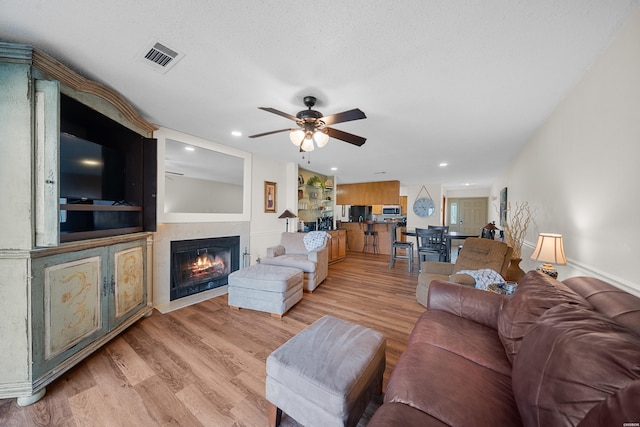 living area featuring light wood-style flooring, visible vents, ceiling fan, and a glass covered fireplace