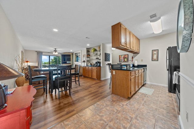 kitchen with dishwasher, dark countertops, brown cabinets, freestanding refrigerator, and a peninsula