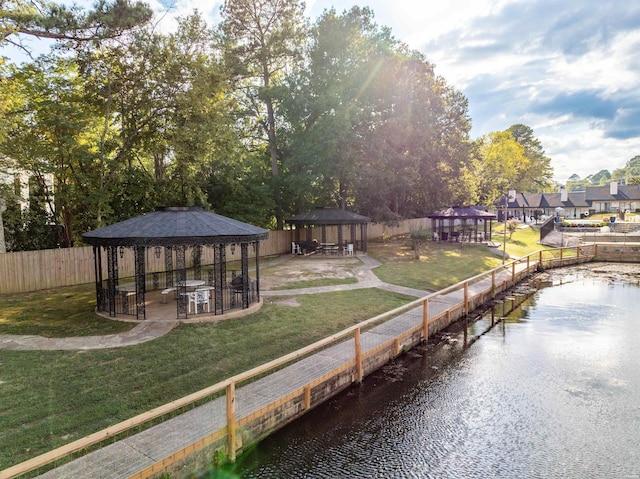 view of dock with a water view, fence, a lawn, and a gazebo