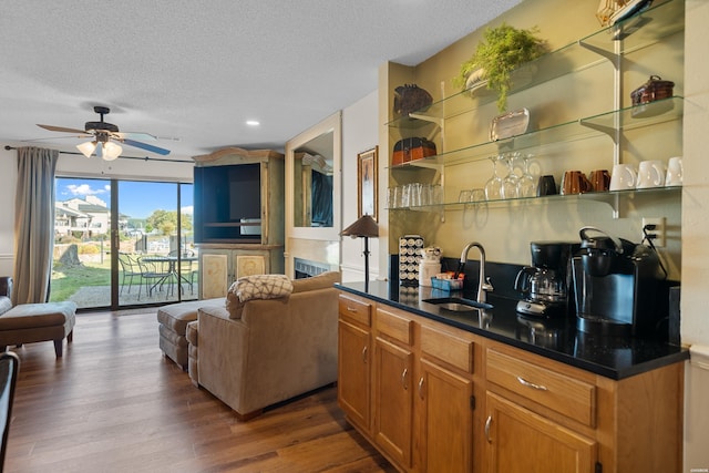 interior space with ceiling fan, a sink, a textured ceiling, wood finished floors, and wet bar