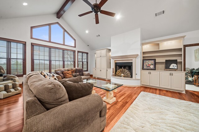 living room featuring high vaulted ceiling, visible vents, a fireplace with raised hearth, and light wood finished floors