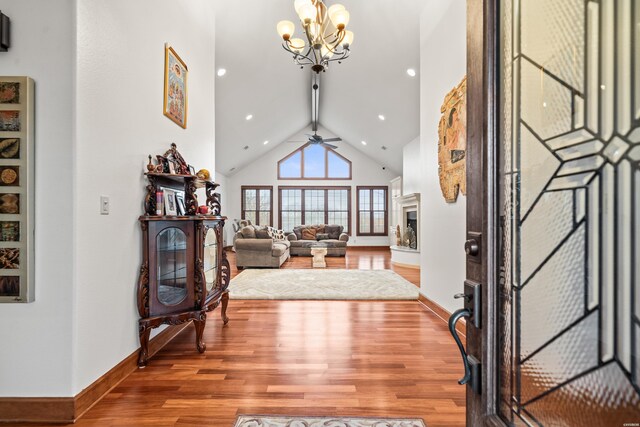 foyer with a fireplace with raised hearth, high vaulted ceiling, ceiling fan with notable chandelier, wood finished floors, and baseboards