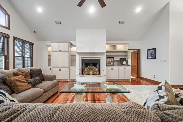 living room featuring a fireplace with raised hearth, high vaulted ceiling, visible vents, and light wood-style flooring