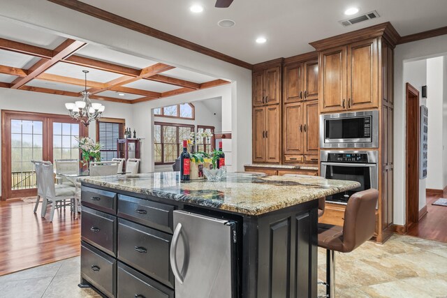 kitchen featuring light stone countertops, stainless steel appliances, a center island, visible vents, and brown cabinets