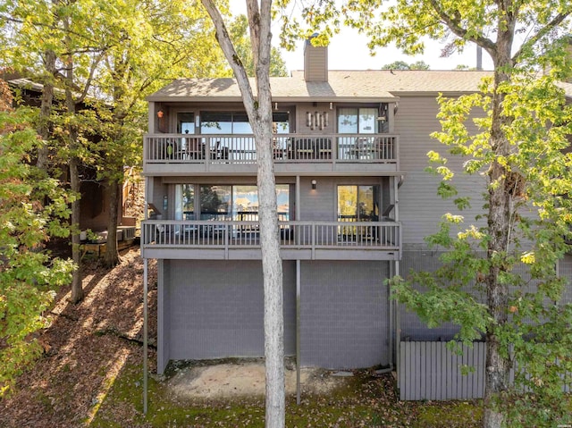 back of house featuring a chimney, an attached garage, and a balcony