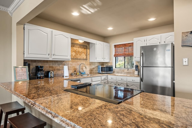 kitchen with light stone countertops, appliances with stainless steel finishes, white cabinets, and a sink