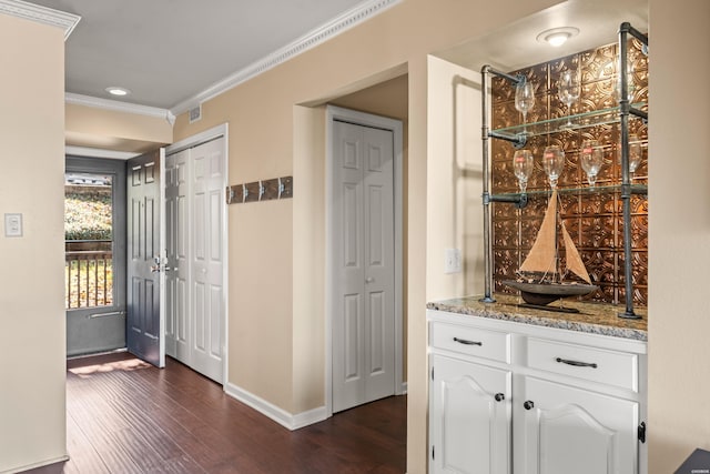 interior space featuring baseboards, white cabinets, dark wood-type flooring, light stone countertops, and crown molding