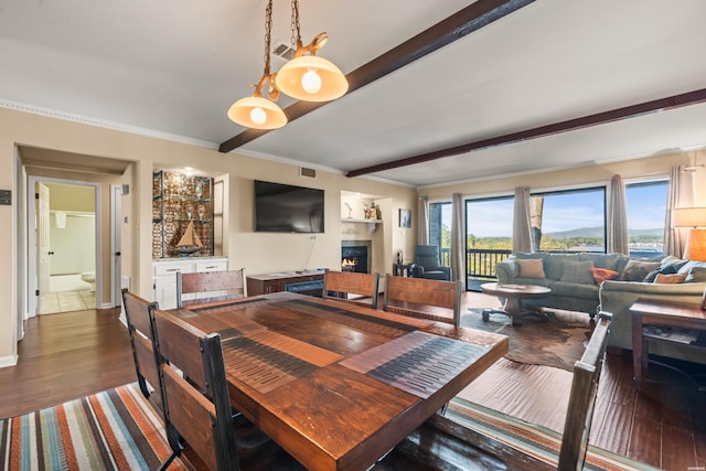 dining room with dark wood-type flooring, a warm lit fireplace, beamed ceiling, and baseboards