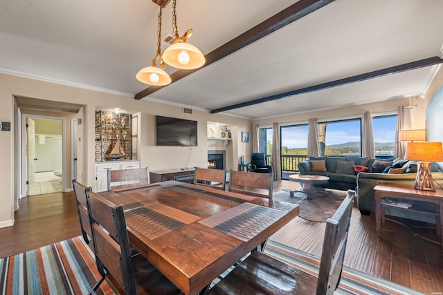 dining area with a lit fireplace, beam ceiling, crown molding, and dark wood-style flooring