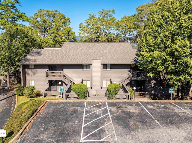 exterior space featuring stairs, uncovered parking, and roof with shingles