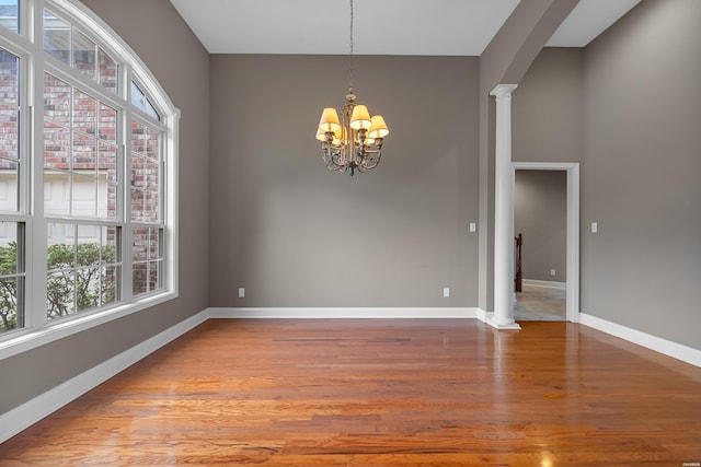 empty room featuring arched walkways, wood finished floors, baseboards, plenty of natural light, and ornate columns