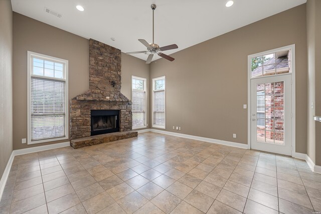 unfurnished living room featuring a stone fireplace, light tile patterned flooring, a ceiling fan, visible vents, and baseboards
