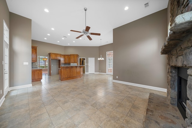 unfurnished living room featuring a stone fireplace, ceiling fan with notable chandelier, a high ceiling, visible vents, and baseboards