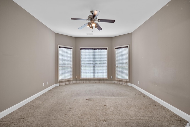 carpeted spare room featuring baseboards and a ceiling fan