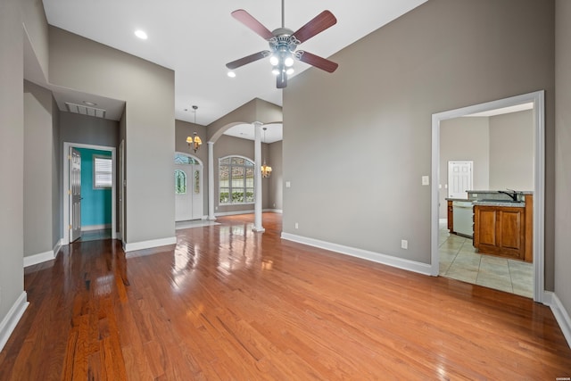 unfurnished living room with arched walkways, a sink, light wood-type flooring, baseboards, and ceiling fan with notable chandelier