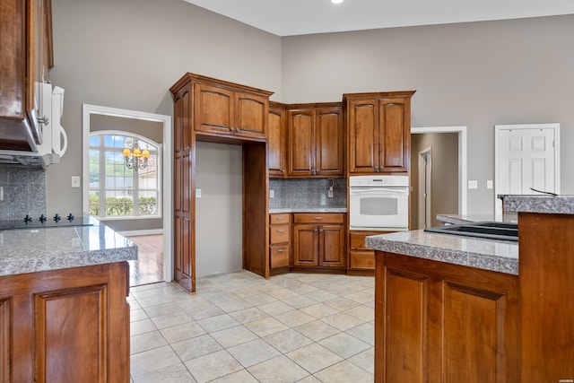 kitchen with light tile patterned floors, oven, tile counters, brown cabinets, and tasteful backsplash