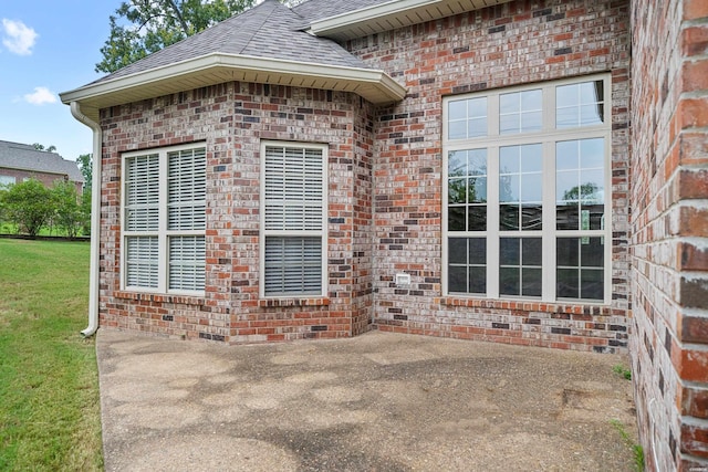 exterior space with a patio area, a shingled roof, a lawn, and brick siding