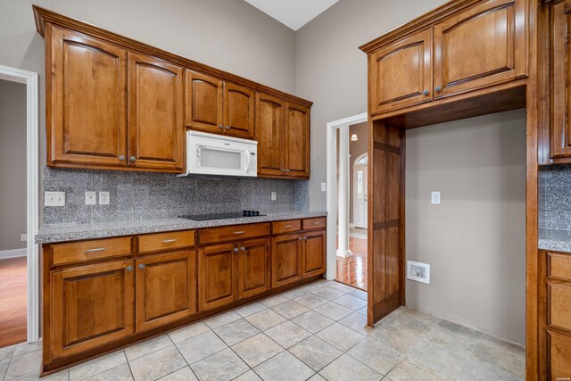 kitchen featuring brown cabinetry, light stone countertops, decorative backsplash, and white microwave