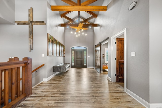 entryway with a barn door, baseboards, wood finished floors, high vaulted ceiling, and beam ceiling