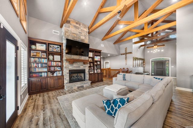 living room with high vaulted ceiling, a stone fireplace, wood finished floors, and beam ceiling